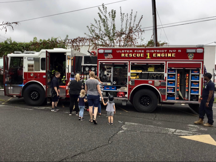 Participants of the library program observe and ask questions about Ulster Hose Engine 1 with Lieutenant Hassett and firefighter Evans-Wright looking on.